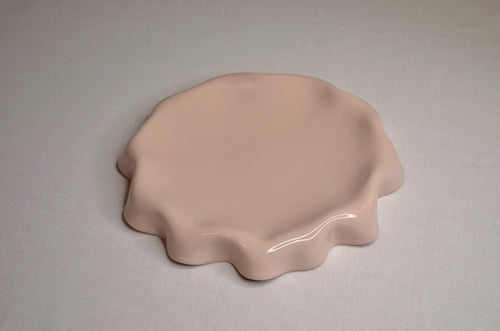 Assiette rose poudré aux bords ondulés.