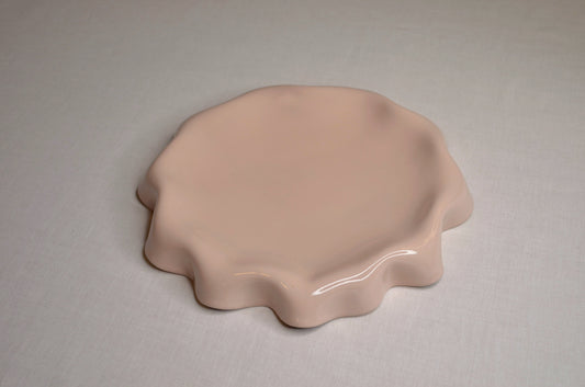 Assiette rose poudré aux bords ondulés.