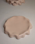 Assiette rose poudré aux bords ondulés.