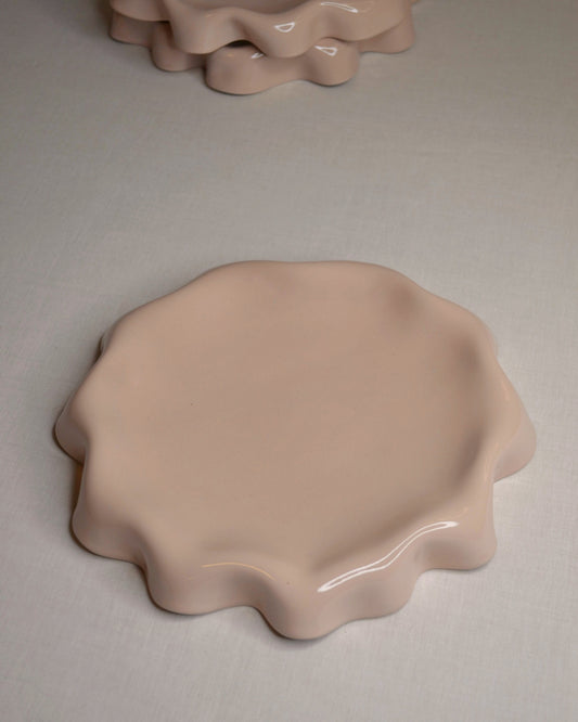 Assiette rose poudré aux bords ondulés.