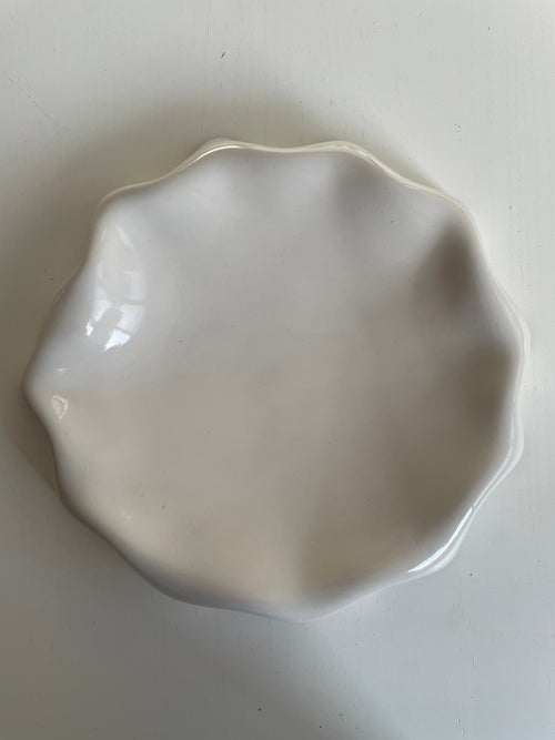 Assiette blanc cassé aux bords ondulés.